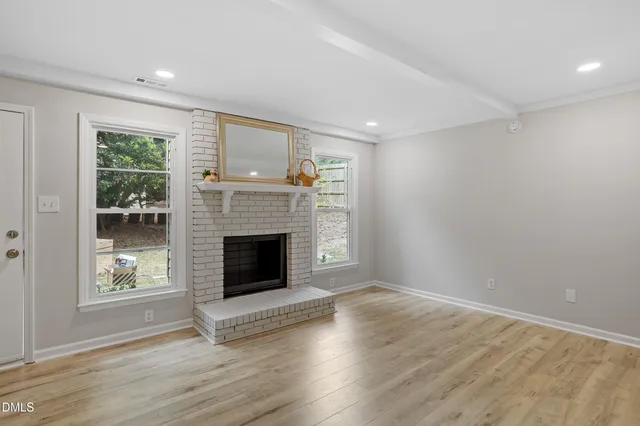 a view of an empty room with wooden floor fireplace and a window