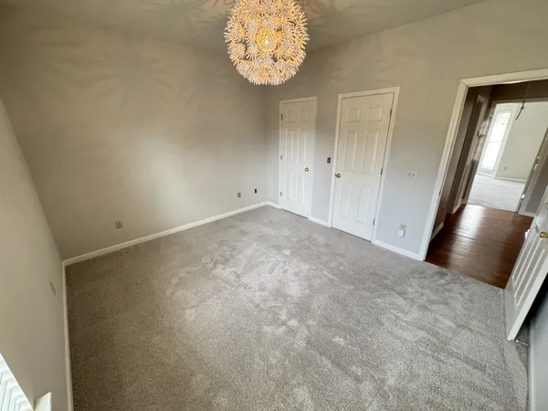 an empty room with a chandelier fan and wooden floor
