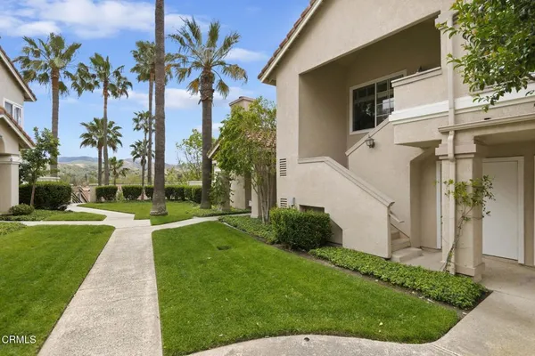 a view of a white house with a big yard potted plants and palm trees