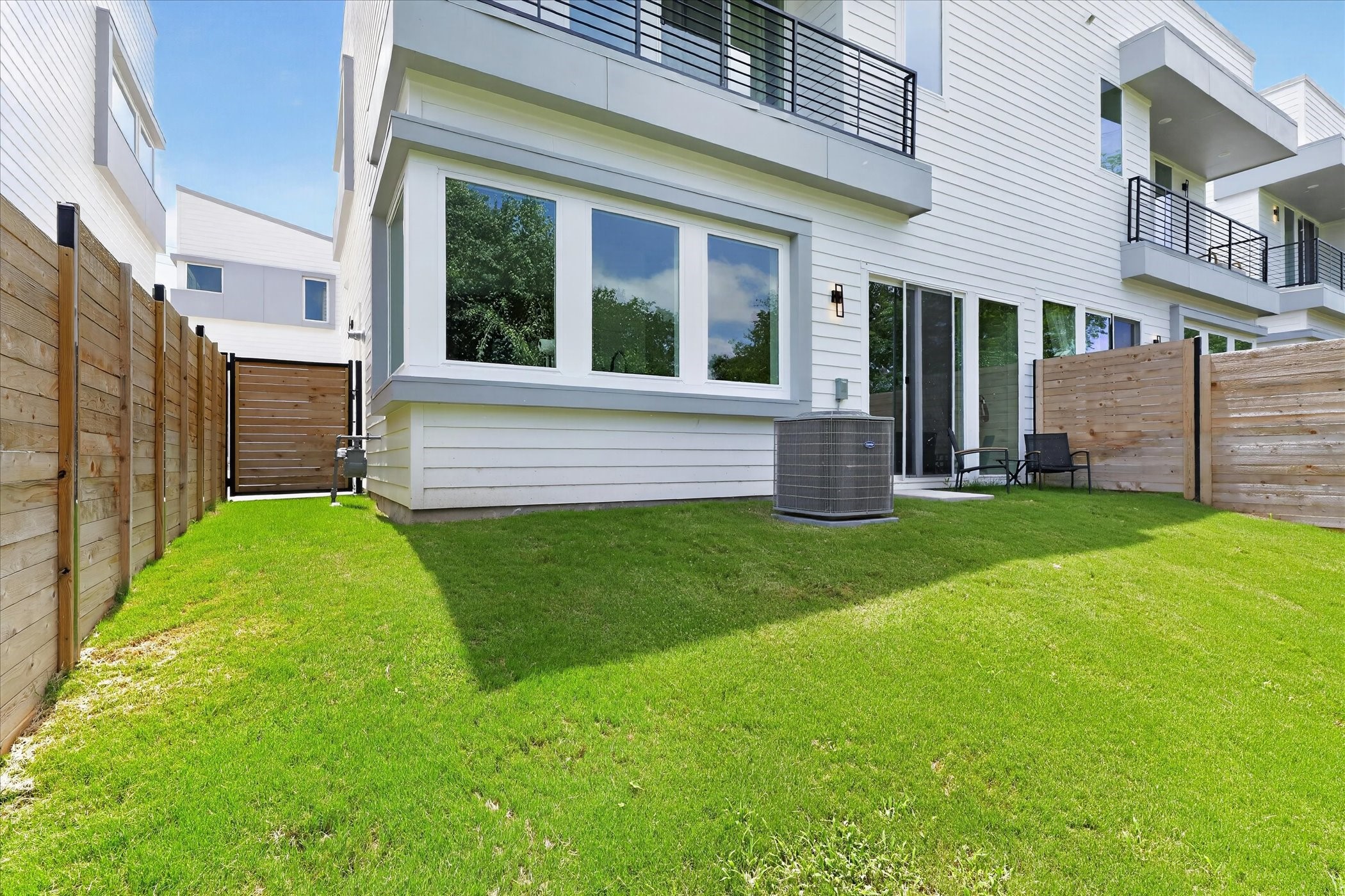2000 Riverside Farms Road, Unit 8101 Austin, TX 78741 - Photo 37 of 41 Modern townhouse exterior with a small, fenced backyard featuring lush grass. Large windows and sliding glass doors offer ample natural light and outdoor access.