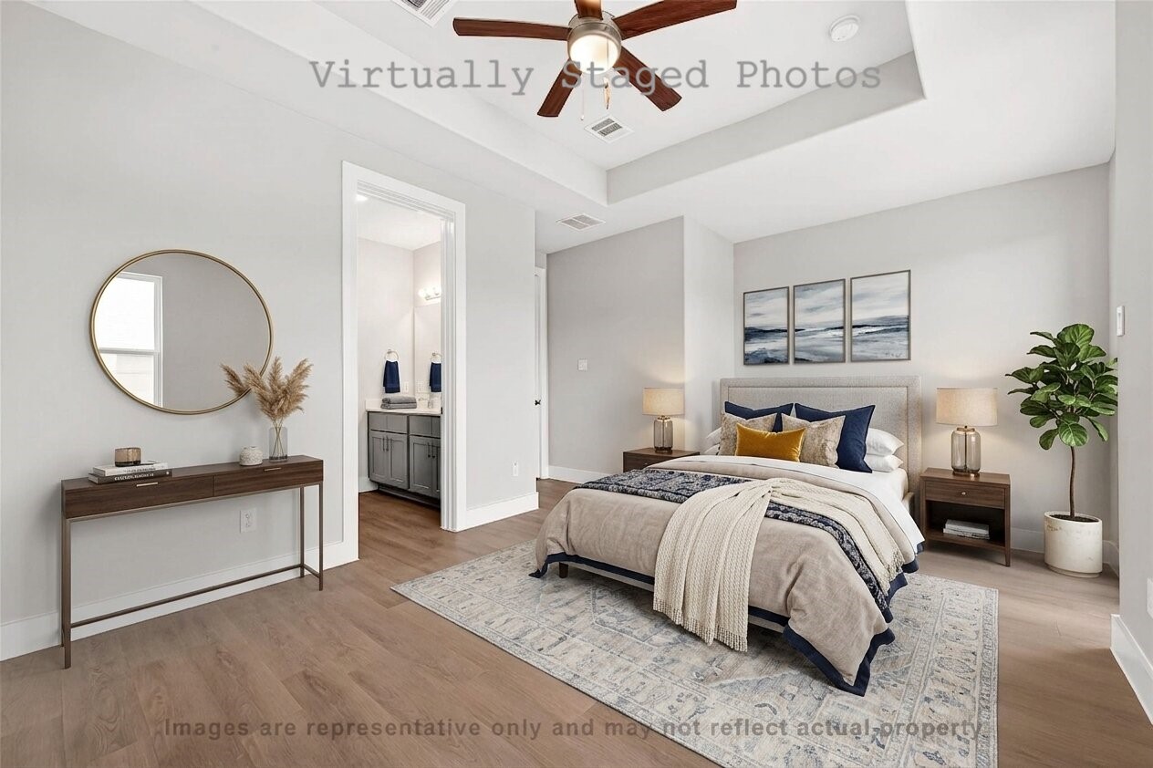 10719 Mason Road, Unit 26 Richmond, TX 77406 - Photo 5 of 50 Virtual Staging - Spacious bedroom features a cozy bed with deep blue accents, a sleek console table with a large round mirror, and an open doorway leading to an en-suite bathroom