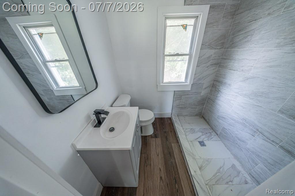 18486 Trinity Street Detroit, MI 48219 - Photo 15 of 19 Modern bathroom featuring a contemporary vanity with a matte black faucet, wood-finish flooring, a white-framed window, and a tiled shower enclosure with a matching tiled floor