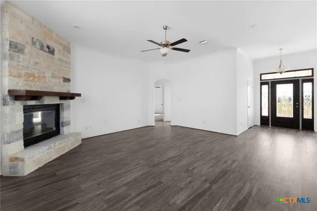 an empty room with wooden floor a ceiling fan a fireplace and windows