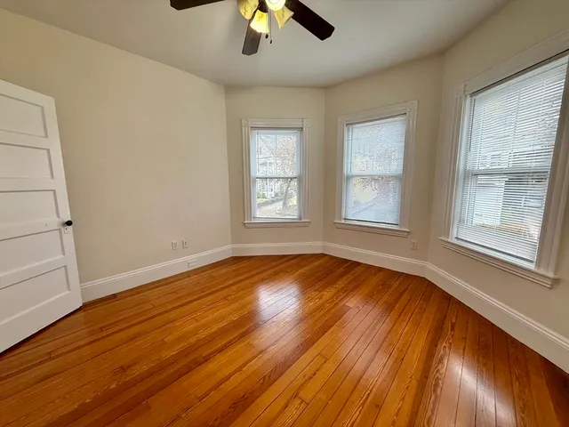 an empty room with wooden floor chandelier fan and windows