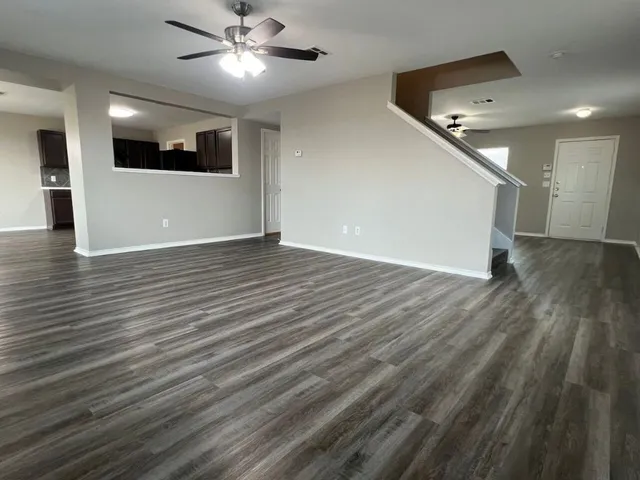 a view of an empty room with wooden floor and a kitchen