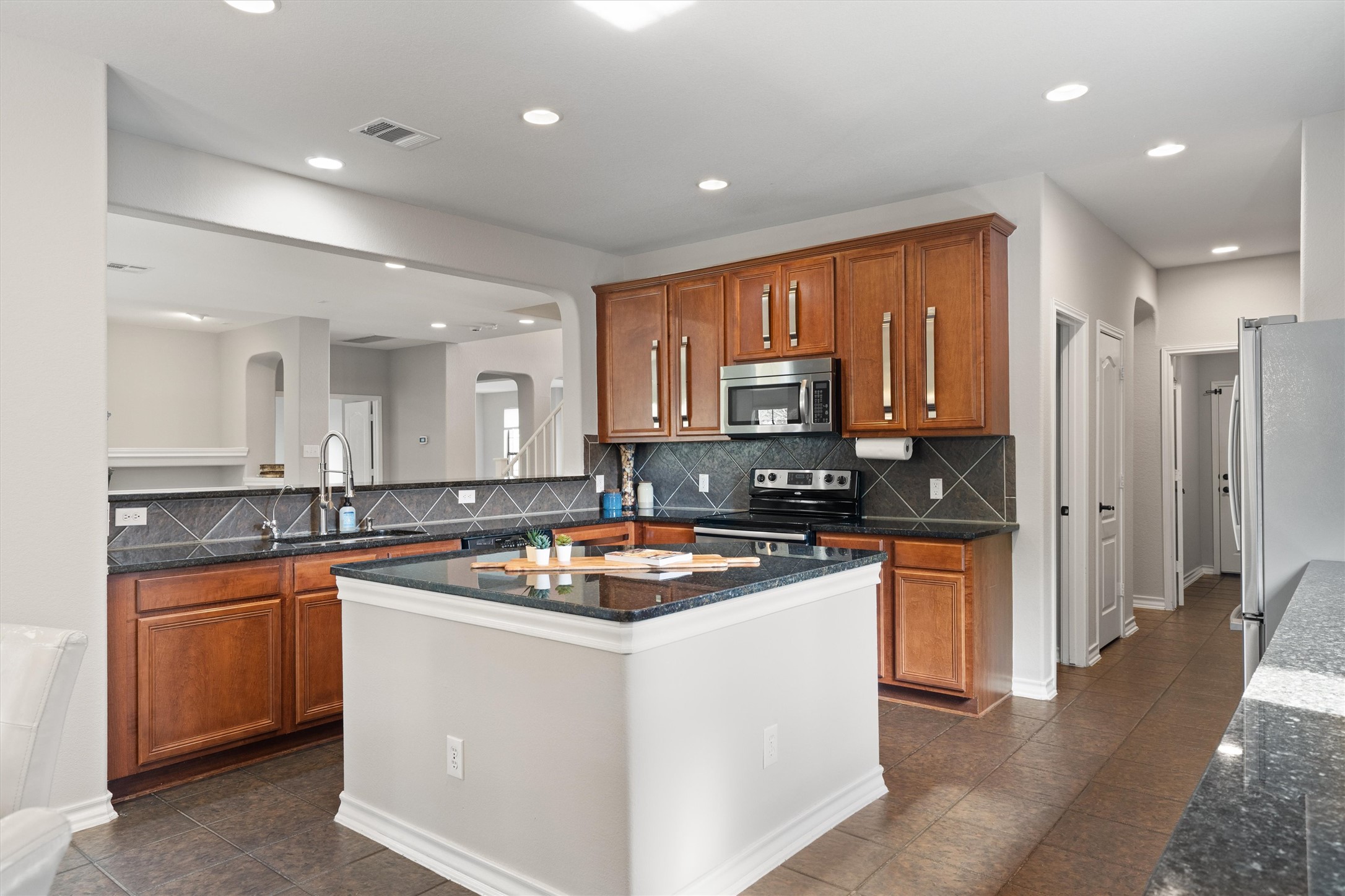 101 Breakaway Road Cedar Park, TX 78613 - Photo 12 of 37 Kitchen featuring arched walkways, wood finish cabinetry, stainless steel appliances, dark stone counters, and recessed lighting