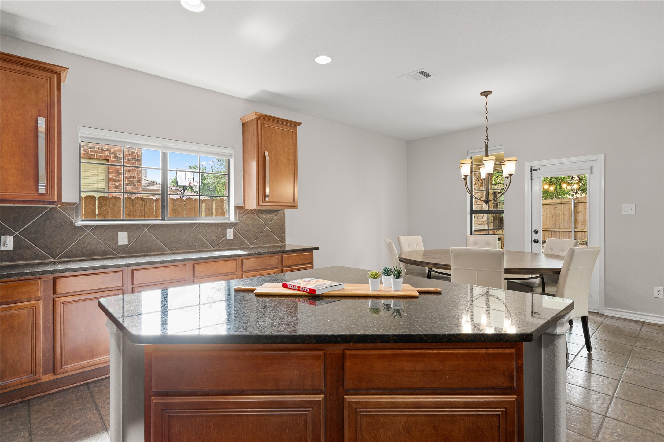 101 Breakaway Road Cedar Park, TX 78613 - Photo 15 of 37 Kitchen with a kitchen island, wood finish cabinetry, tasteful backsplash, dark stone countertops, and plenty of natural light