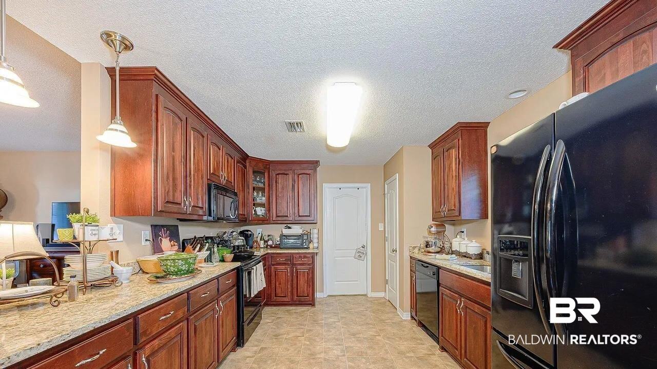 12230 Bromley Road Stapleton, AL 36578 - Photo 16 of 34 Kitchen with black appliances, decorative light fixtures, a textured ceiling, light stone countertops, and glass insert cabinets