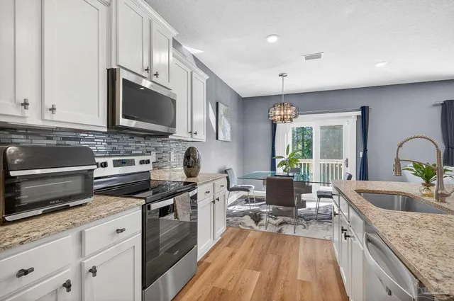 a kitchen with stainless steel appliances granite countertop a stove a sink a refrigerator white cabinets and wooden floor