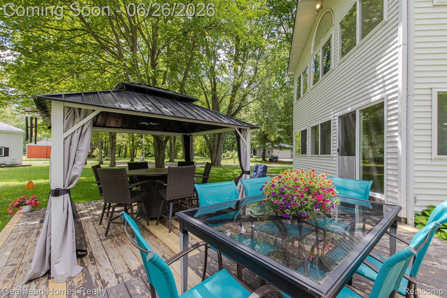 12364 Morrish Road Clio, MI 48420 - Photo 72 of 81 Spacious rear deck featuring a dark metal gazebo, mature trees, and a multi-level white siding exterior with numerous windows and a sliding glass door