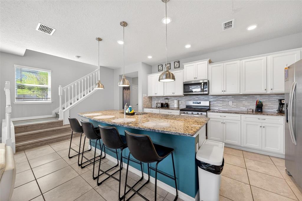 7554 Oak Spring Lane Davenport, FL 33837 - Photo 20 of 74 a kitchen with stainless steel appliances kitchen island granite countertop a table chairs sink and cabinets