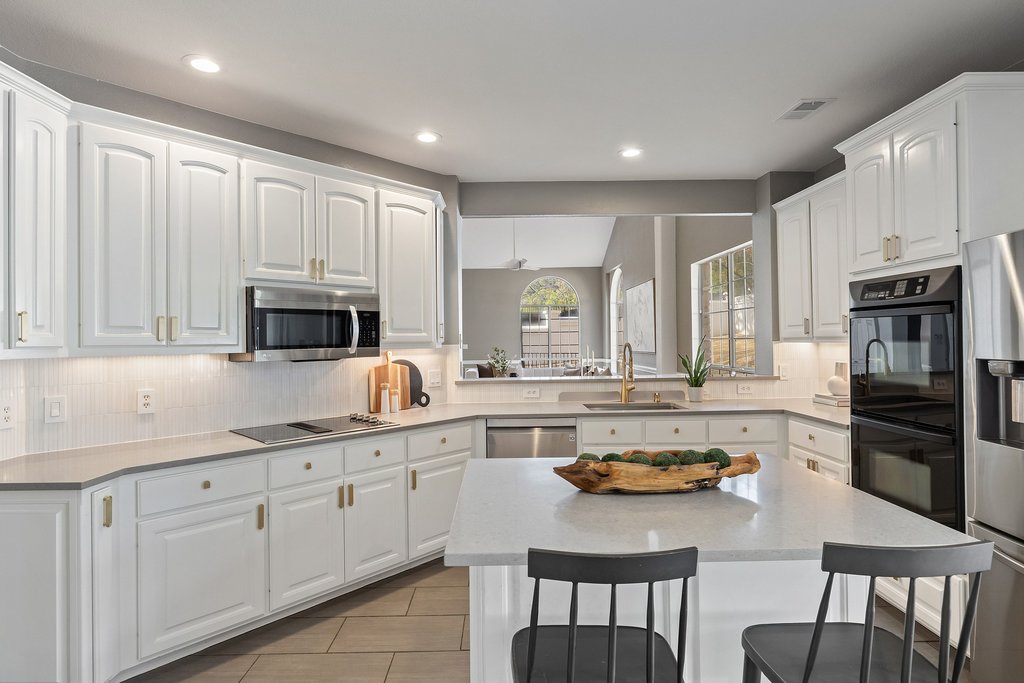 1815 Rue De St Tropez Austin, TX 78746 - Photo 12 of 39 Kitchen featuring black appliances, decorative backsplash, white cabinets, a kitchen bar, and a kitchen island