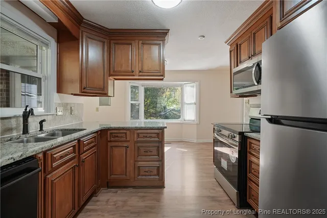 a kitchen with stainless steel appliances granite countertop a refrigerator a sink dishwasher a stove with wooden cabinets and floor