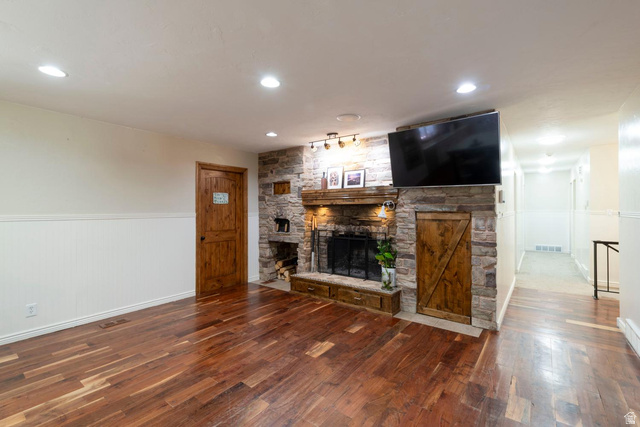 9676 Mt Jordan Road Sandy, UT 84092 - Photo 18 of 38 Living space featuring a stone-clad fireplace with wood mantle, wood-finish flooring, recessed lighting, and white wainscoting