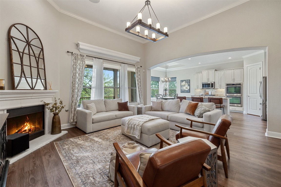 Living room featuring an inviting chandelier, arched walkways, crown molding, and a lit fireplace