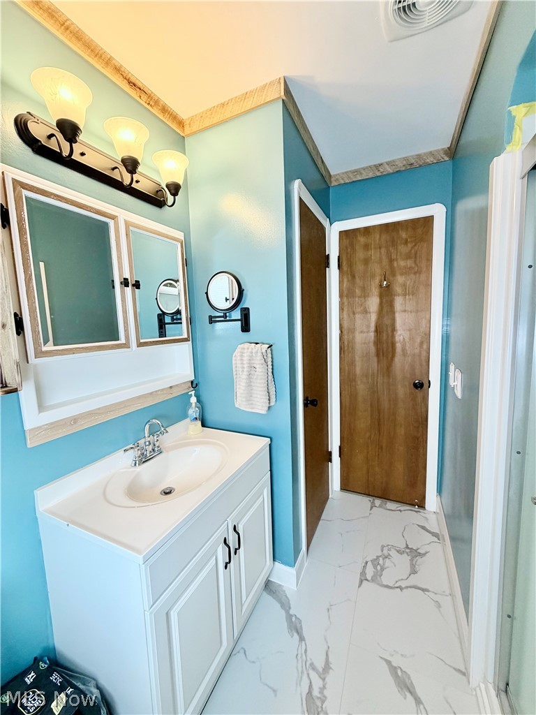 32125 Densmore Road Willowick, OH 44095 - Photo 13 of 23 Bathroom featuring a white vanity with panel door fronts, a medicine cabinet with mirrored doors, a three-light vanity fixture, a wood-finish door, and marble-look flooring