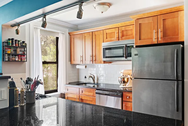 a kitchen with stainless steel appliances granite countertop a refrigerator a stove and a sink with wooden floors