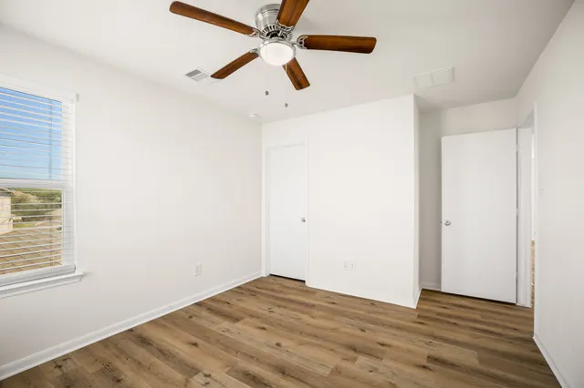 an empty room with wooden floor ceiling fan and windows