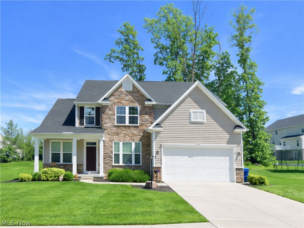 Stone and siding exterior with a dark shingled roof, featuring a covered entry porch, a paved driveway, and an integrated two-car garage