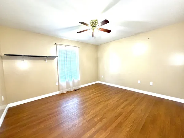 an empty room with wooden floor fan and windows