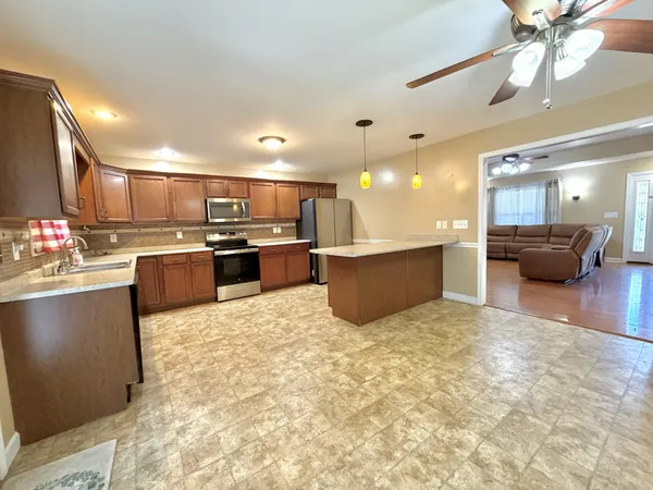 a kitchen with stainless steel appliances kitchen island granite countertop a stove top oven a sink a dining table and chairs with wooden floor