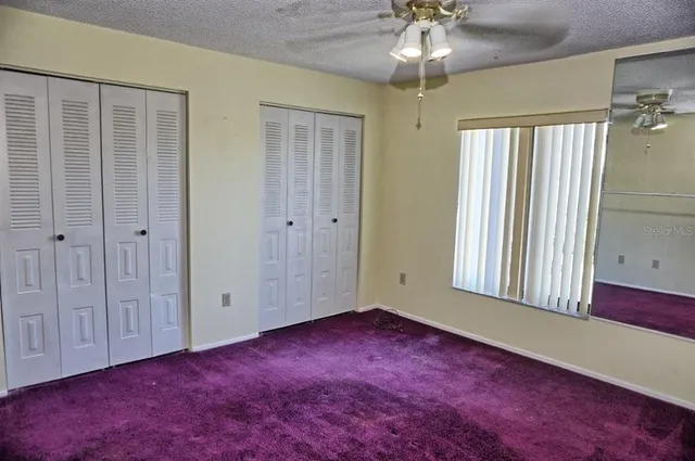 an empty room with chandelier fan and windows