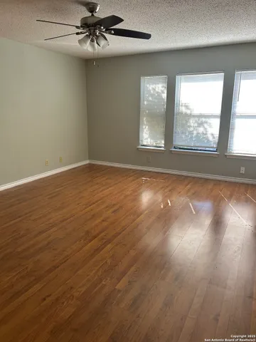 an empty room with wooden floor fan and windows