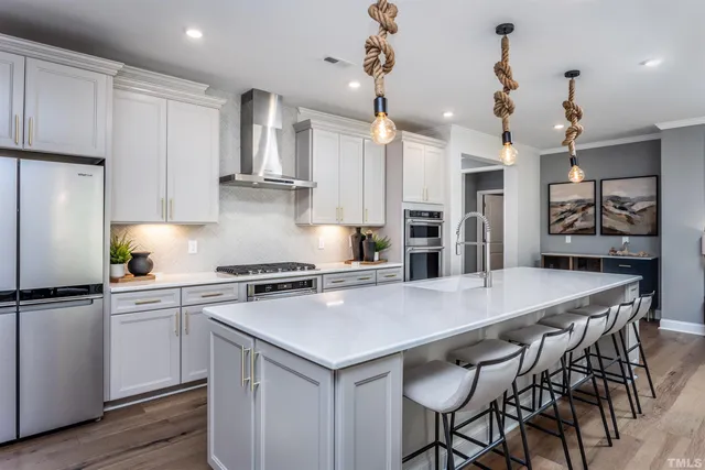 a kitchen with stainless steel appliances a stove a refrigerator a sink a dining table and chairs with wooden floor