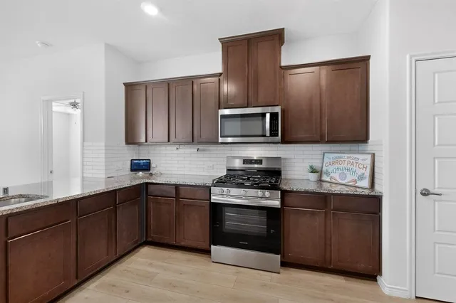 a kitchen with stainless steel appliances granite countertop a stove top oven a sink dishwasher and a refrigerator with wooden cabinets