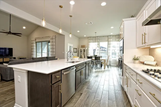 a kitchen with stainless steel appliances granite countertop a stove top oven a sink dishwasher a dining table and chairs with wooden floor