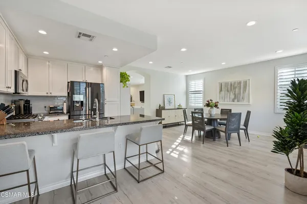 a kitchen with stainless steel appliances granite countertop dining table chairs refrigerator and sink