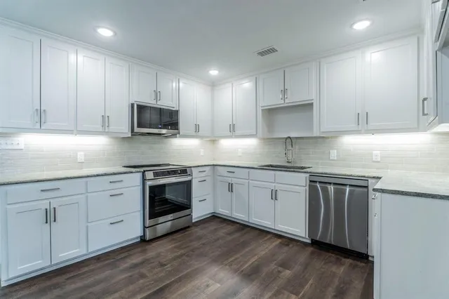 a kitchen with stainless steel appliances granite countertop a stove top oven a sink and white cabinets