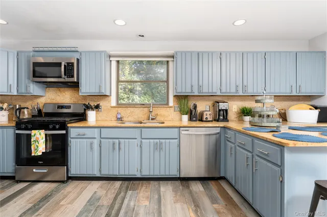 a kitchen with stainless steel appliances granite countertop wooden cabinets a sink a stove a microwave and wooden floors