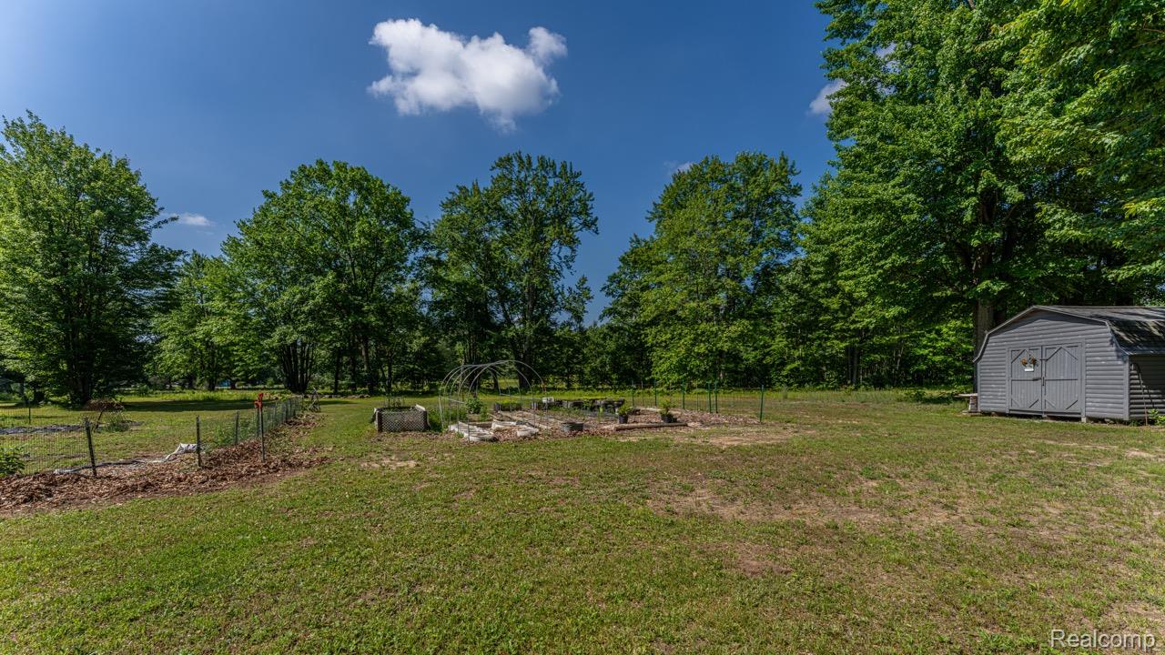 2418 South 41st Road South Cadillac, MI 49601 - Photo 53 of 57 Expansive exterior grounds featuring a gray storage shed, established garden beds, a partial wire fence line, and mature trees creating a natural border
