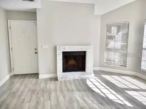 an empty room with wooden floor fireplace and windows
