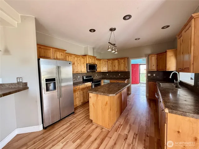 a kitchen with stainless steel appliances granite countertop a refrigerator a sink dishwasher a stove and a dining table with wooden floor