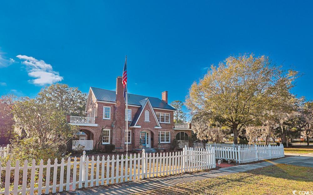 Tudor house with a chimney, a fenced front yard, and brick siding