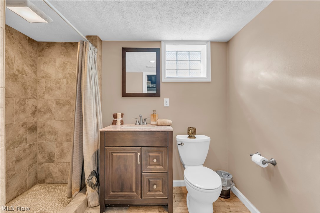 3023 Norris Avenue Cleveland, OH 44134 - Photo 31 of 41 Bathroom featuring a shower with stone tile walls and a pebble floor, a single vanity with a stone countertop, and a glass block window