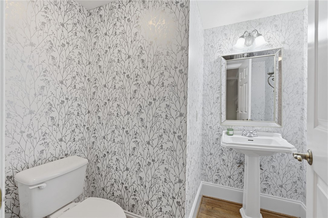204 Butler Avenue Greenville, SC 29601 - Photo 18 of 26 Elegant powder room with a sleek pedestal sink, decorative mirror, and patterned wall covering.