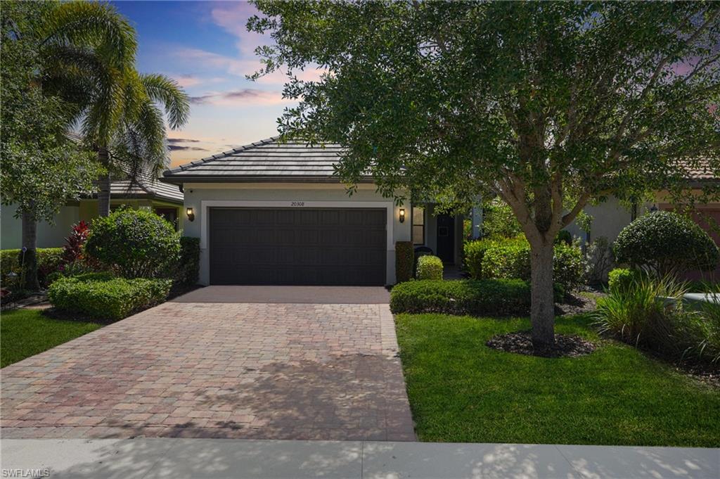 View of front of house with decorative driveway, an attached garage, stucco siding, and a front yard
