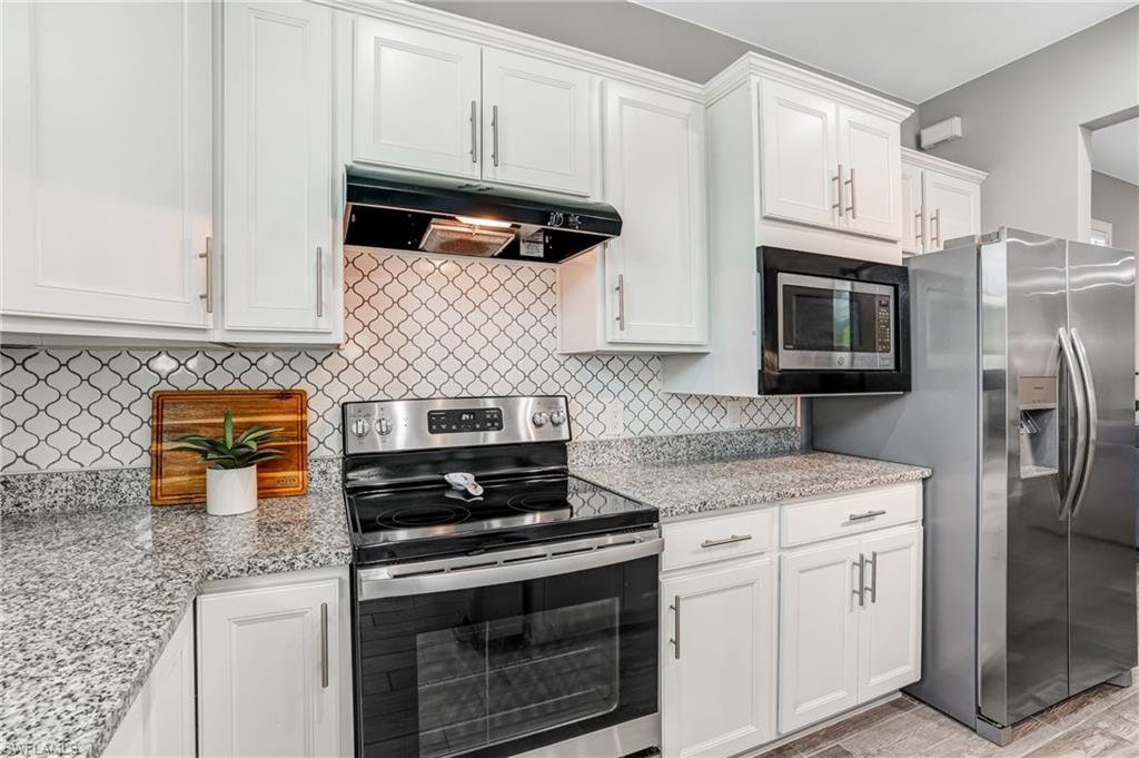 20308 Corkscrew Shores Boulevard Estero, FL 33928 - Photo 11 of 47 Kitchen featuring stainless steel appliances, under cabinet range hood, white cabinets, and tasteful backsplash