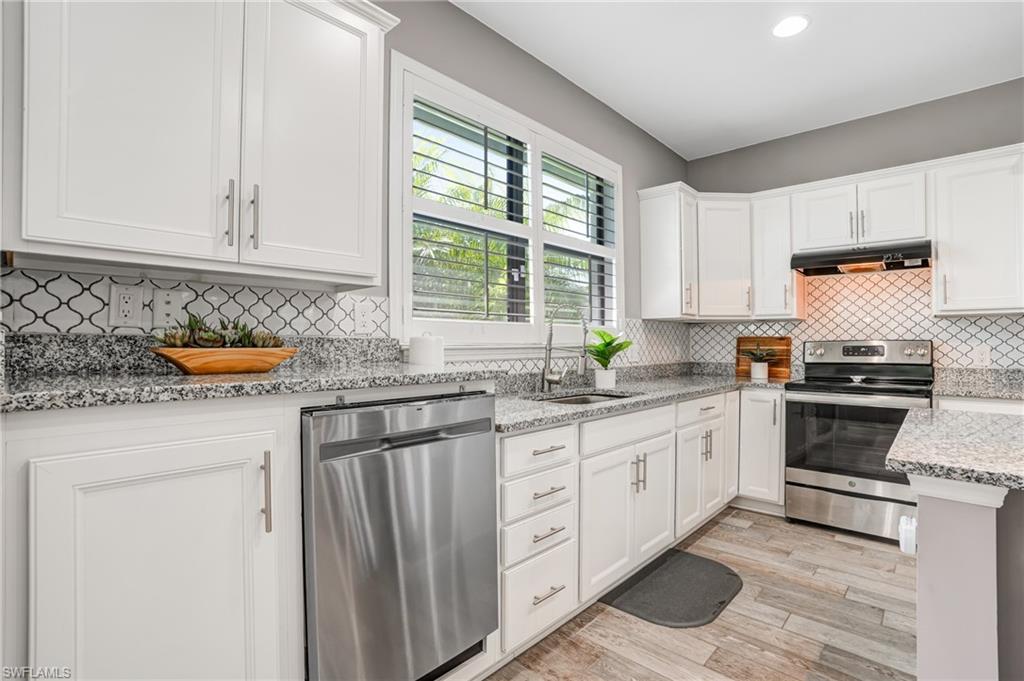 20308 Corkscrew Shores Boulevard Estero, FL 33928 - Photo 12 of 47 Kitchen with appliances with stainless steel finishes, a sink, under cabinet range hood, white cabinetry, and light wood-type flooring