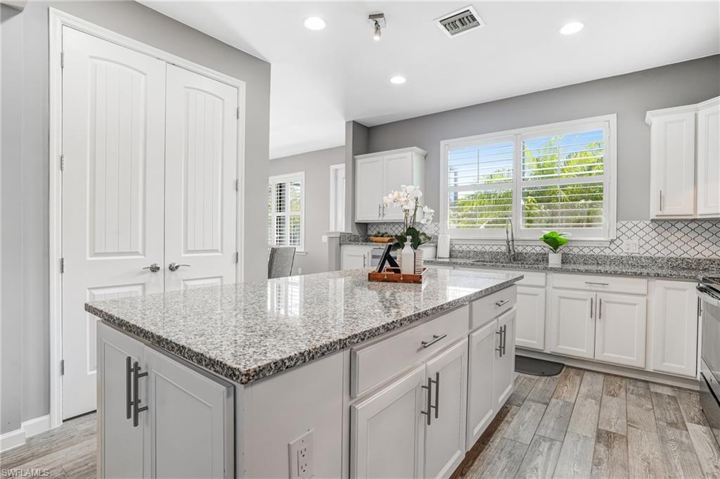20308 Corkscrew Shores Boulevard Estero, FL 33928 - Photo 10 of 47 Kitchen with a sink, light wood-style flooring, a kitchen island, backsplash, and white cabinetry