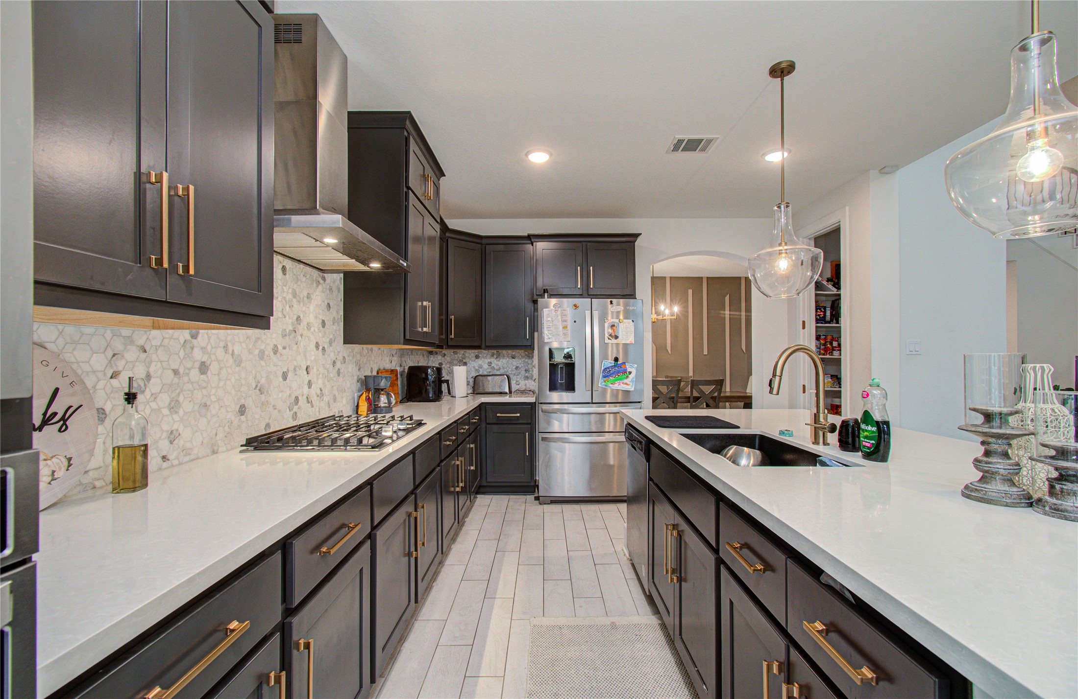 4211 Limestone Terrace Manvel, TX 77578 - Photo 10 of 33 This modern kitchen features dark cabinetry, sleek white countertops, and a stylish backsplash. It includes stainless steel appliances, a gas cooktop, and pendant lighting, creating a sophisticated and functional space.
