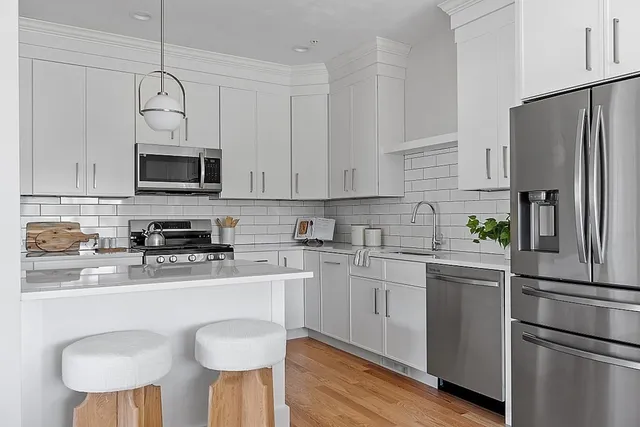 a kitchen with stainless steel appliances granite countertop a refrigerator a stove a sink dishwasher and white cabinets with wooden floor