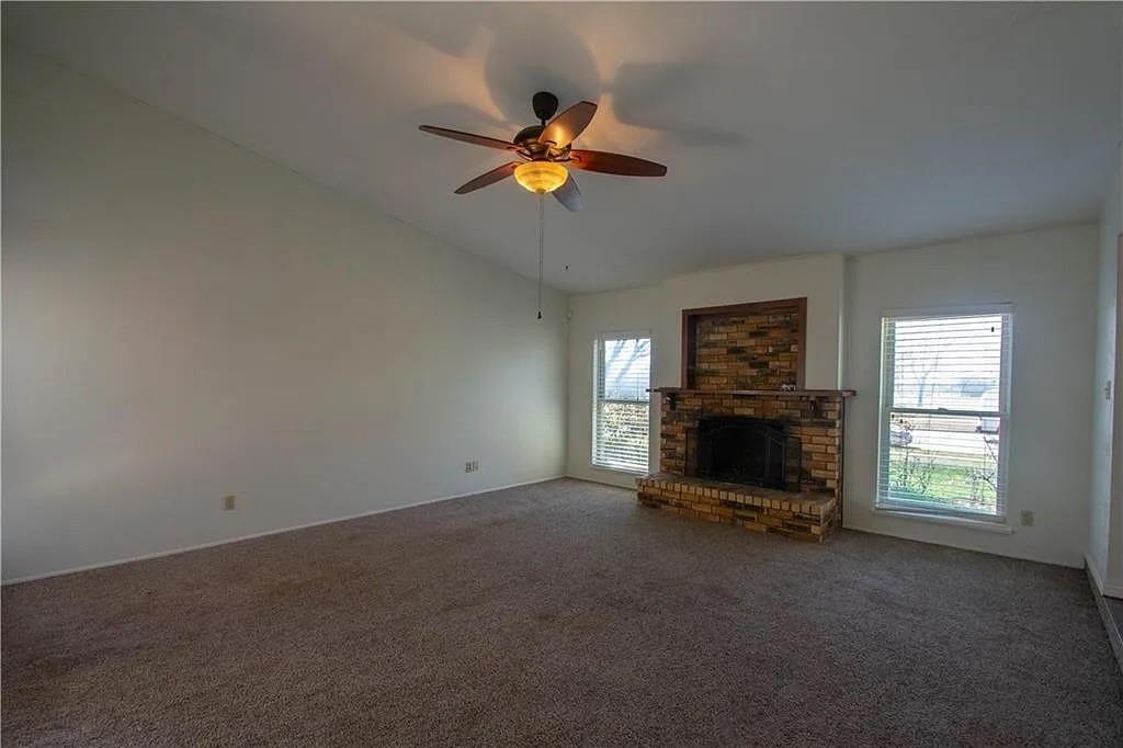 6500 Blue Ridge Trail Plano, TX 75023 - Photo 8 of 14 Living space featuring a brick fireplace with hearth, two windows with blinds, a ceiling fan with integrated lighting, vaulted ceilings, and carpet flooring