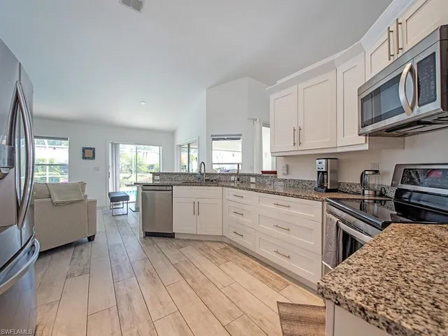 a kitchen with stainless steel appliances granite countertop a stove top oven a sink dishwasher and white cabinets with wooden floor