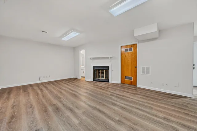 an empty room with wooden floor fireplace and windows