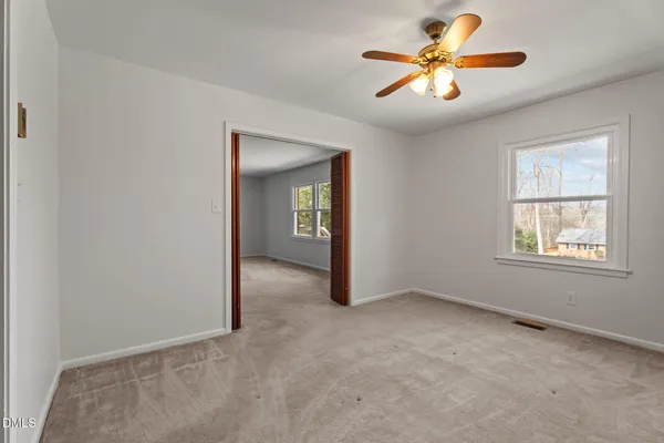 an empty room with chandelier fan and windows
