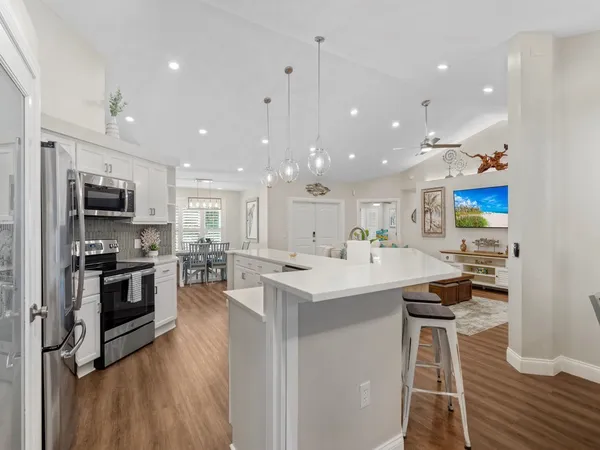 a kitchen with stainless steel appliances kitchen island granite countertop a stove top oven a sink a dining table and chairs with wooden floor